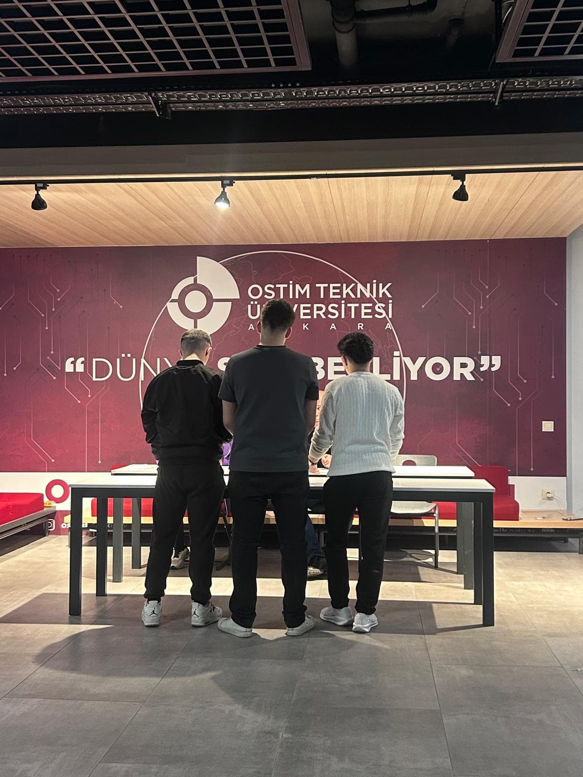 Maestrobot 2026 yarışmasında OSTİM Teknik Üniversitesi Ankara panosunun önünde masada çalışan üç yarışmacı